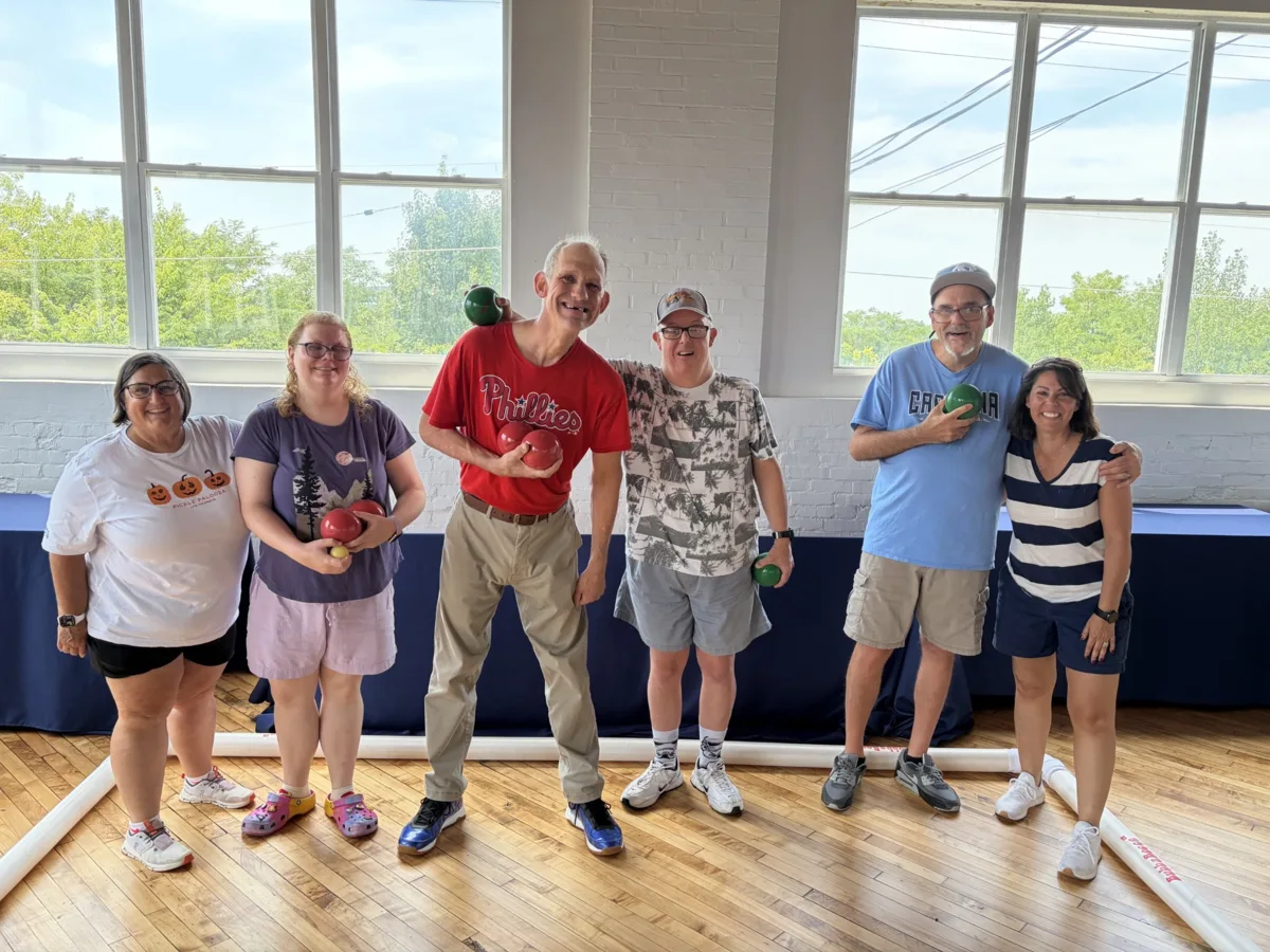 Clubhouse Living members and friends smiling with bocce balls in the sunlit gym